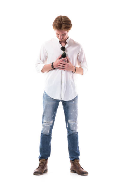 istock Serious young man in white shirt and jeans looking down holding hand and getting dressed 1255243851