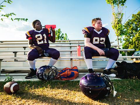Two Junior Football player drinking water from the bottle during practice at the outdoor field.