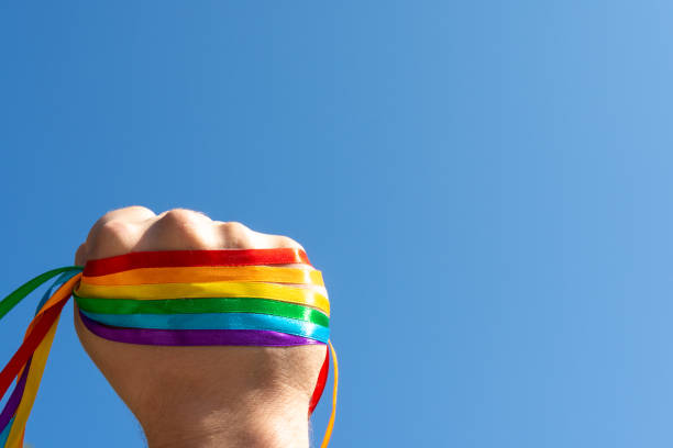 mano alzata contro il cielo in segno di unità e forza braccialetto bandiera arcobaleno lgbt - gay pride wristband rainbow lgbt foto e immagini stock
