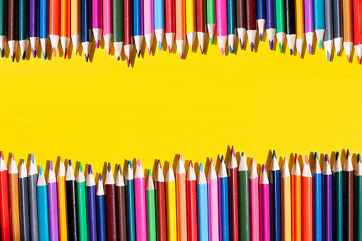 colored pencils lie next to each other in the form of a fence on a yellow background. Flat lay. Top view.