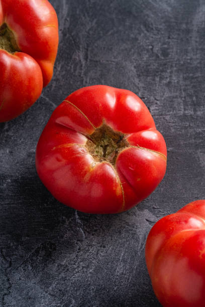 trois légumes roses de tomate d’héritage dans la rangée, les tomates mûres rouges fraîches, la nourriture végétalienne, le fond en béton de pierre foncée, la vue d’angle - tomato beefsteak tomato heirloom tomato pink photos et images de collection