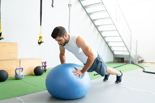 Latin young man doing push-ups on fitness ball during cross-training at gym