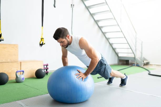 Active Man Doing Workout At Health Club Latin young man doing push-ups on fitness ball during cross-training at gym fitness ball photos stock pictures, royalty-free photos & images