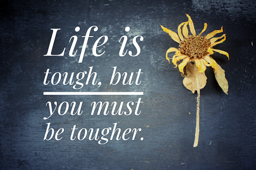 Inspirational quote - Life is tough, but you must be tougher. Motivational words concept with  text message on blackboard and a dried sunflower head decoration background.