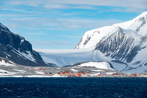 Long mountain range surrounded by vast ice sheet rising above sea; even bigger mountains in background