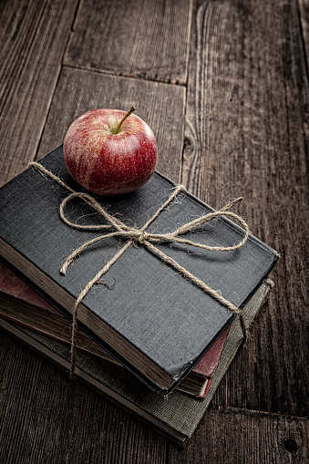 This is a photograph of a red apple on top of a stack of old retro books held together with twine sitting on top of a old retro wooden table