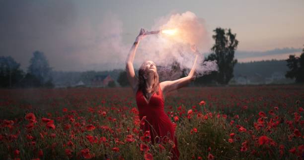 porträtt av vacker brunett flicka i en röd klänning dansar med röd brinnande signal flare i vallmo fält - happy slowmotion bildbanksfoton och bilder