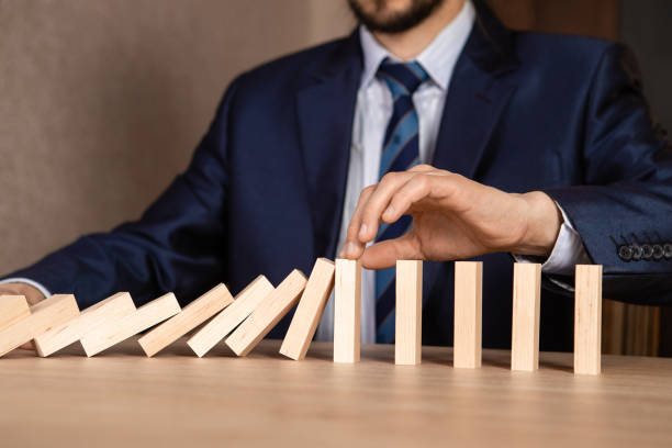 istock Businessman hand Stopping Falling wooden Dominoes effect from continuous toppled or risk, strategy and successful intervention concept for business. 1255285291