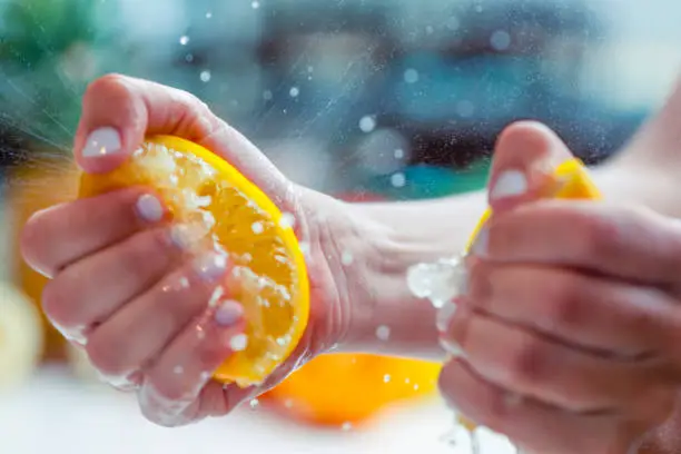 Woman squeezing the juice from a lemon. Some droplets of juice can be seen. Two halves of the lemon can be seen.