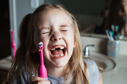 Cute snaggletoothed girl laughs after brushing her teeth at home in bathroom
