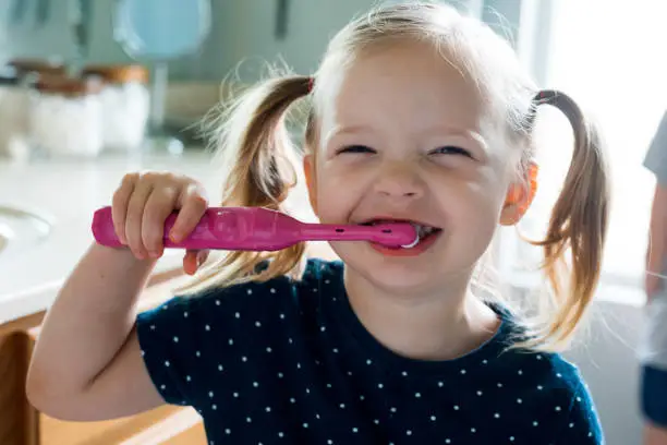 Toddler girl brushes teeth with electric toothbrush at home in bathroom