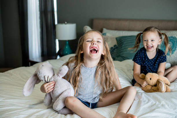istock Cute elementary age sisters play with stuffed animals at home on bed 1255285512