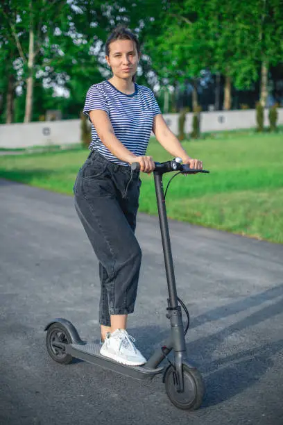 A vertical view of a brunette having fun on a sunny day on her scooter. She is wearing casual black jeans and a t-shirt on the stripes.
