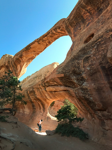 Hiker young man in sun spotlight through a window on the walls of red clay rock canyon standing in front of  Incredible Double-O-Arch,Arches National Park. take a rest enjoying view at destination