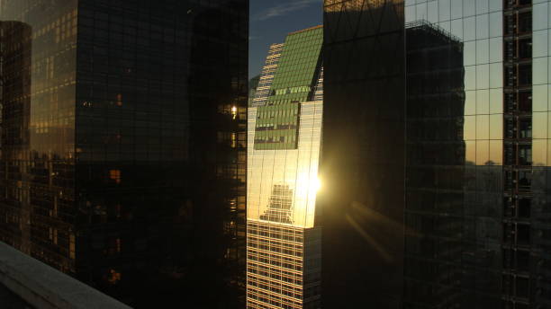 istock Glass windows of a commercial skyscraper reflecting the sunset light, placed between dark towers of a financial district 1255304397