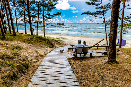 Happy couple of seniors are sitting near a sandy beach of the Baltic Sea