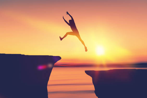 istock Silhouette man jumping between cliff at tropical sunset beach. Freedom challenge and travel adventure concept. 1255329228