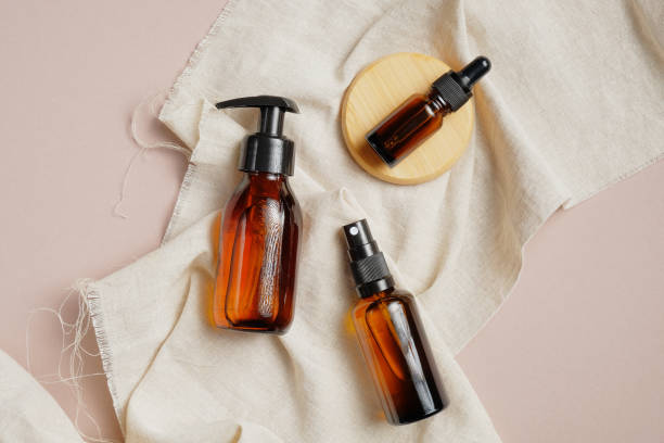 istock Amber glass cosmetic packaging set without labels. Flat lay pump bottle dispenser, dropper bottle and spray on beige fabric. Top view, overhead. Beauty product design mockup. 1255332241