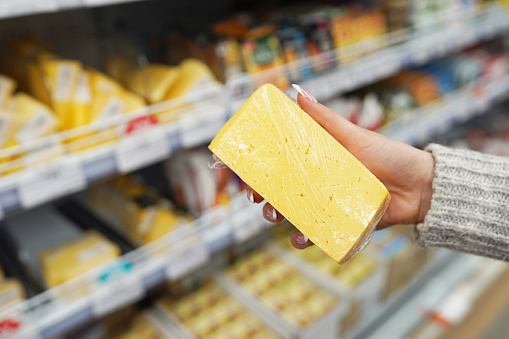 Female hand is holding cheese in the supermarket