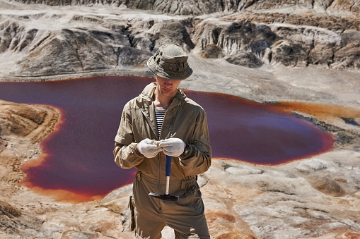 field expedition geologist examines a sample of a mineral against the backdrop of a canyon with a red salt lake
