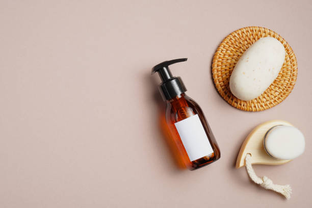 istock Bathroom accessories and beauty products on beige background. Flat lay composition with natural soap, amber glass bottle with shampoo, facial cleaning brush. 1255337020
