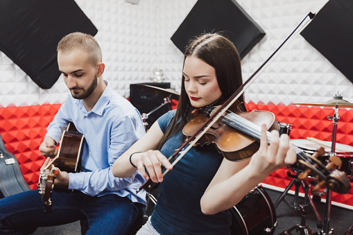 Man and woman playing violin and guitar in a recording studio.