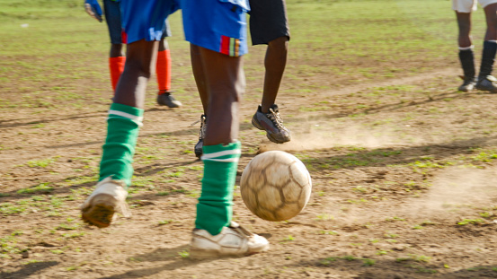 Football feet and a football playing soccer on in a dirt grass dry dusty field in Swaziland Africa.