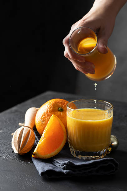 istock Fresh orange juice pouring into the glass with ice on dark background. Refreshment  fruit beverage. 1255346166
