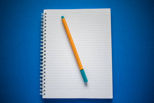 istock Flat lay of notepad and yellow pen on blue background 1255355189