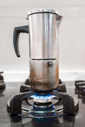 Old coffee maker on a gas stove lit with fire in a kitchen