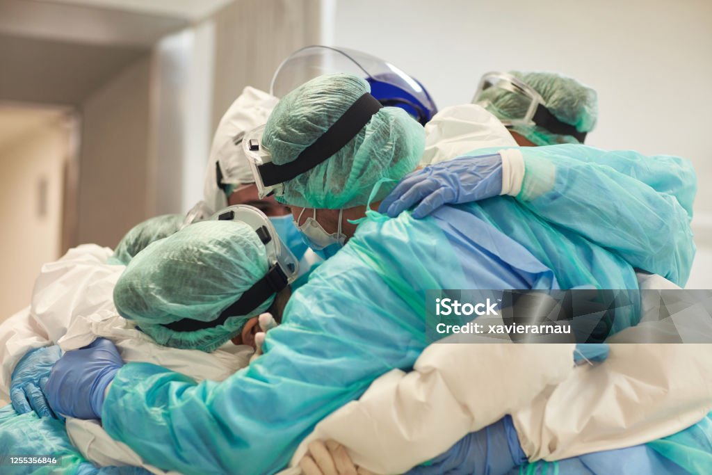 Doctors and Nurses With Arms Around Each Other in Support Partial view of hard-working male and female hospital team in full protective wear standing together in group embrace. Doctor Stock Photo
