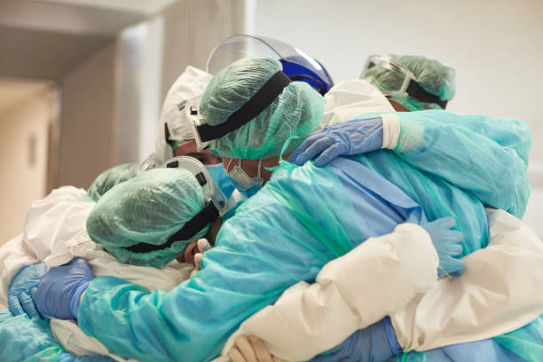 Doctors and Nurses With Arms Around Each Other in Support Partial view of hard-working male and female hospital team in full protective wear standing together in group embrace. real life photos stock pictures, royalty-free photos & images