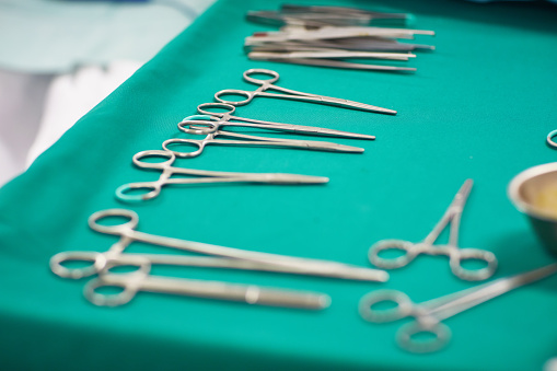 Close-up of various pieces of sterilized surgical equipment laid out on green cloth covering medical tray and ready for medical procedure.