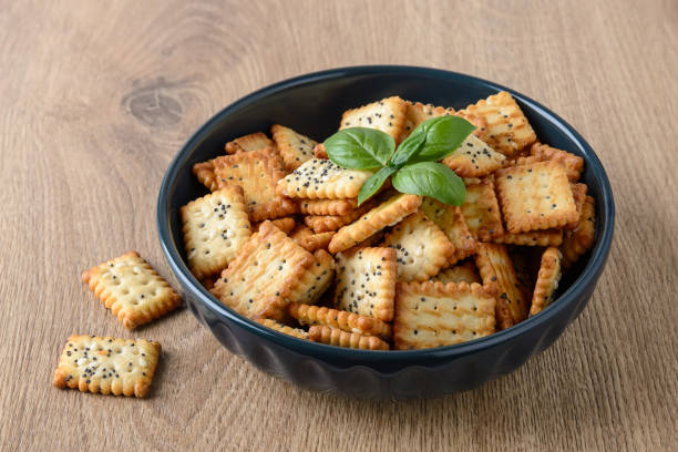 istock Small salty rectangular crackers with poppy and sesame seeds in a dark ceramic bowl on a brown table. Crispy wheat flour snack and beer appetizer. 1255362297