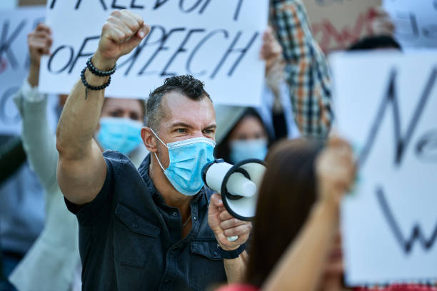 istock Angry activist with raised fist shouting through megaphone on demonstrations during COVID-19 epidemic. 1255362384