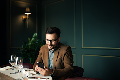 Retrato de un hombre exitoso en la mesa en un restaurante de lujo, usando un teléfono inteligente. photo