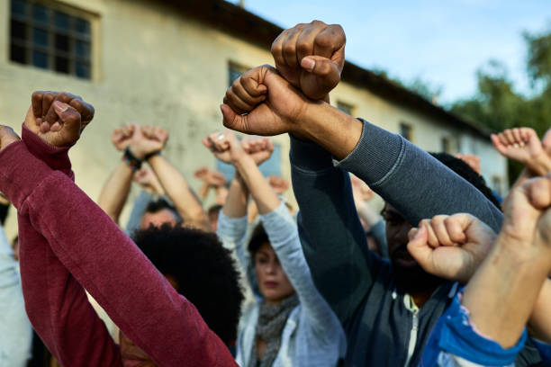 Close-up of crowd of people with clenched fists above head protesting on the streets. Close-up of multi-ethnic group of protesters with arm-crossing gesture on public demonstrations. police brutality photos stock pictures, royalty-free photos & images