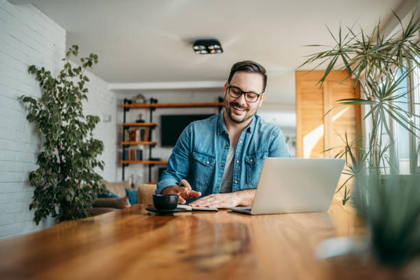 istock Handsome man writing in note pad and using laptop at cozy home, portrait. 1255363287