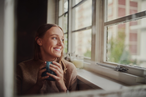 Woman drinking coffee sitting near window sill
