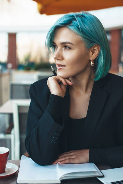 istock Blue haired businesswoman looking away while sitting in a cafeteria and reading a book 1255367814