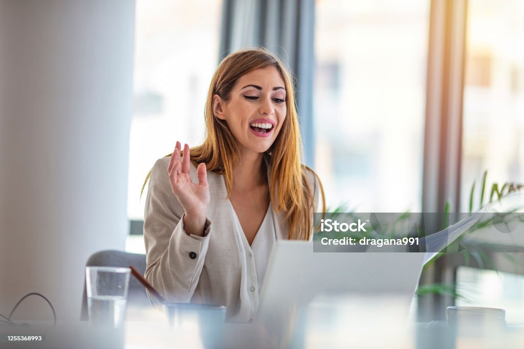 Entrepreneur working on line typing with a laptop at office with a window in the background Beautiful young businesswoman smiles as she participates in a video conference with a colleague. She is using a laptop. Entrepreneur working on line typing with a laptop at office with a window in the background Interview - Event Stock Photo