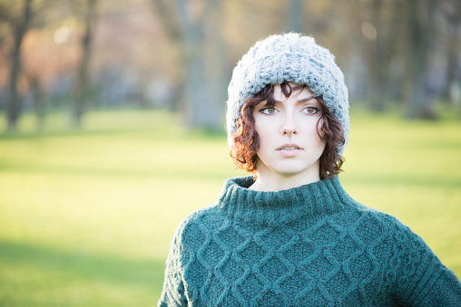 Backlit sunset portrait of young woman wearing a wooly hat and knitted sweater - autumn / winter outdoors.