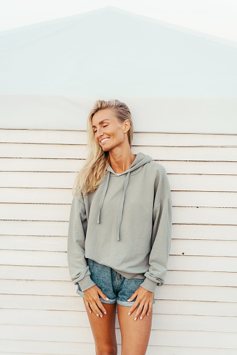 Cute beautiful tanned blonde woman in denim shorts and a stylish hoodie having fun  and sincerely laughs.
