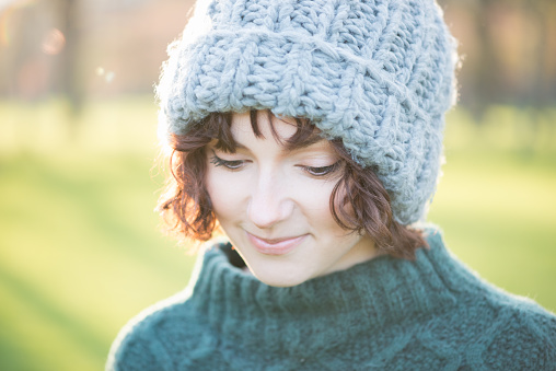 Backlit sunset portrait of young woman wearing a wooly hat and knitted sweater - autumn / winter outdoors.