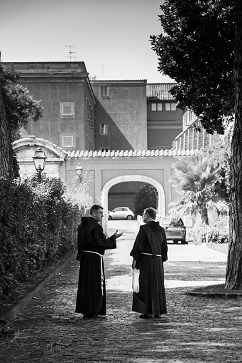 Rome, Italy - August 14, 2015: Monks engaging in daily activity against the background of ancient church and a park. Basilica di San Giovanni in Laterano