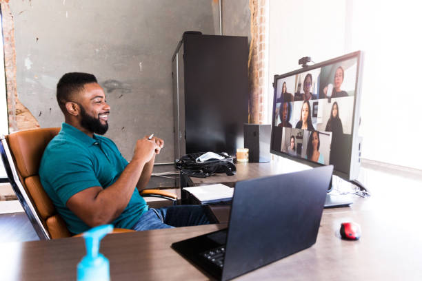 Cheerful businessman video chats with colleagues A mid adult businessman smiles confidently as he talks with a team of associates during a virtual meeting during the COVID-19 pandemic. virtual event stock pictures, royalty-free photos & images