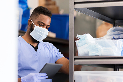 A confident male nurse checks the personal protective equipment inventory in the supply closet of a doctor's office or hospital ward.