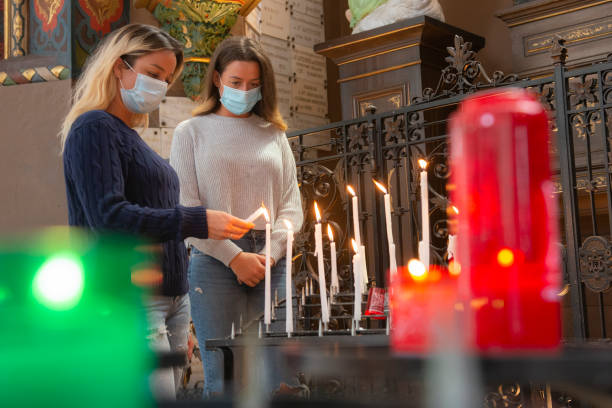 две женщины зажигают свечи внутри церкви во время коронавируса - latin american and hispanic ethnicity church catholicism mission стоковые фото и изображения