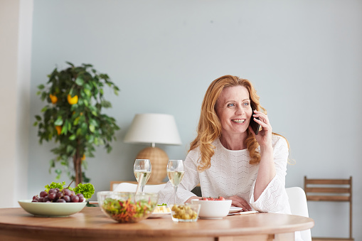 Portrait of elegant mature woman speaking by smartphone while enjoying dinner at home or cafe, copy space