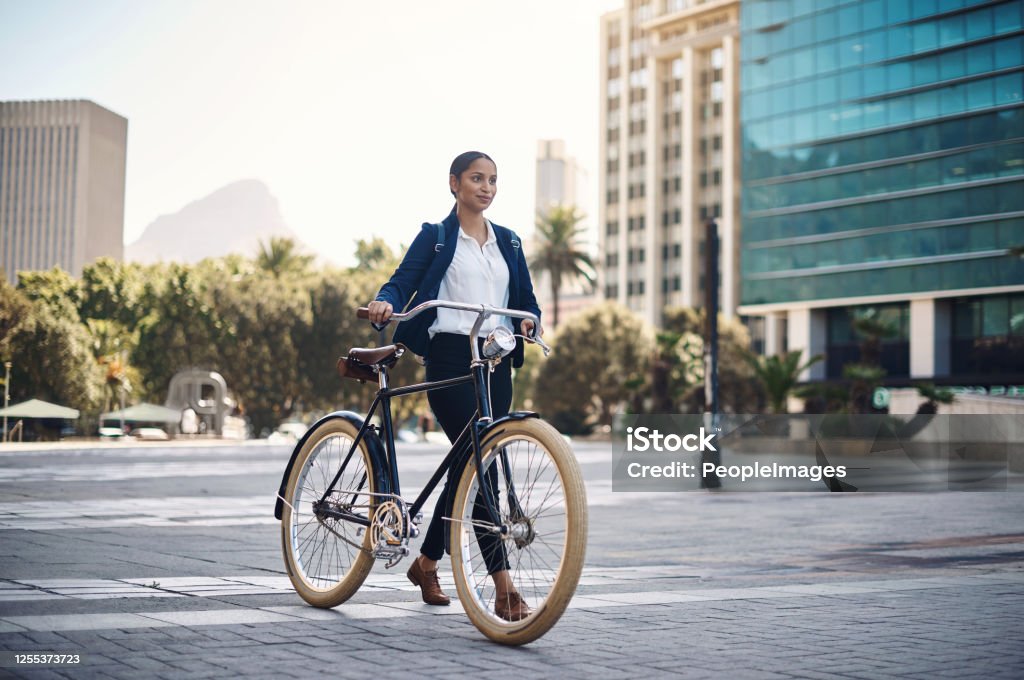 Let ambition lead the way Shot of a young businesswoman traveling with a bicycle through the city Cycling Stock Photo